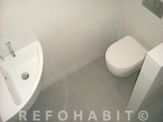 Hacer baño adicional en piso de Horta, Barcelona. Lavamanos esquinero pequeño e inodoro suspendido para ahorrar espacio.